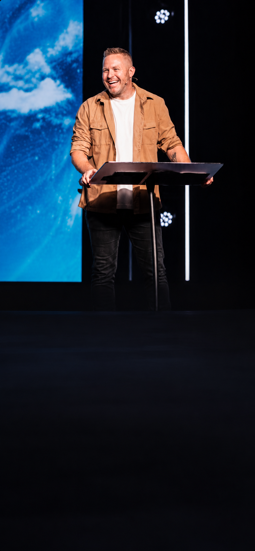 Jason Parks laughing on stage at a podium while speaking to a packed room