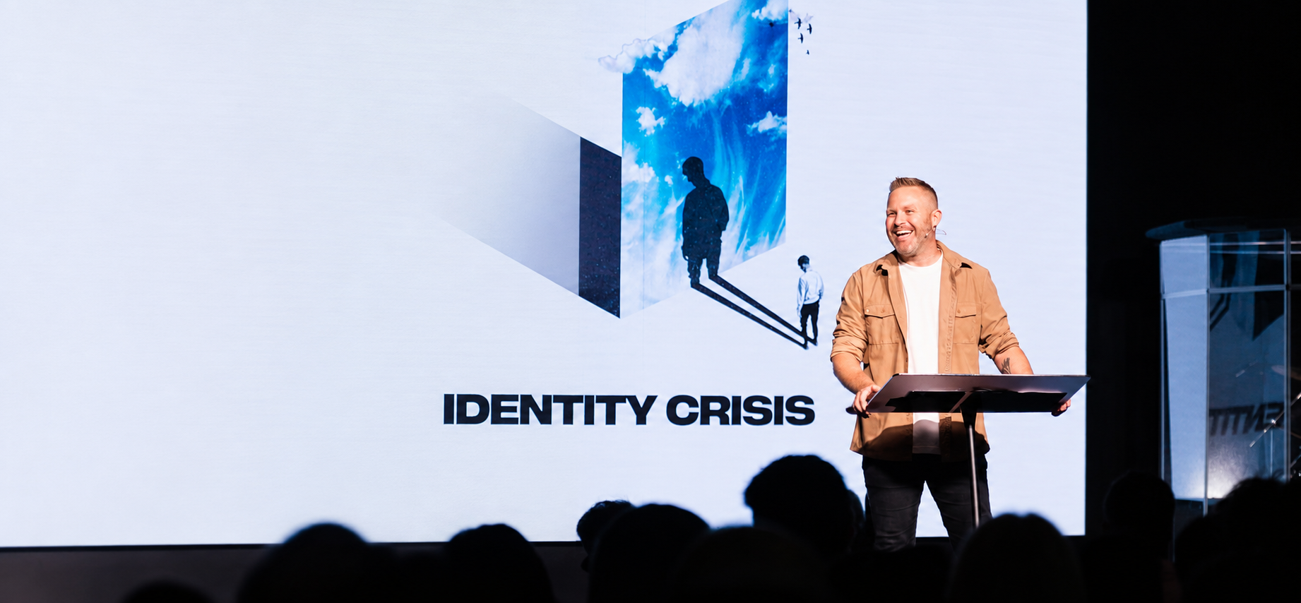 Jason Parks laughing on stage at a podium while speaking to a packed room